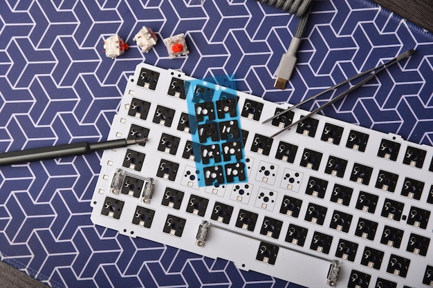Overhead shot of a disassembled mechanical keyboard, revealing the PCB, switches, and mounting plate, with keycaps laid out neatly beside it.