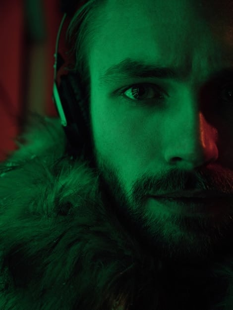 A dark, intense close-up of an esports player's focused face, illuminated by the glow of multiple monitors, with wires and gaming equipment blurred in the background, conveying the concentration of competitive play.