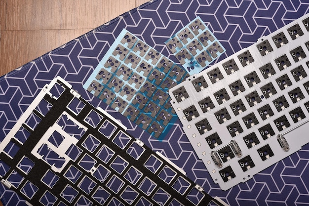 A high-angle shot of various PC components laid out on an anti-static mat, ready for assembly. The components include a motherboard, CPU, RAM sticks, a graphics card, and an NVMe SSD. Tools like screwdrivers and zip ties are also visible.