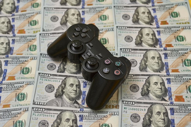 A digital rendering of a dollar bill with a game controller superimposed. The background is blurred to focus on the concept of investment in gaming.