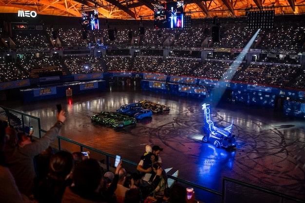 An overview shot of a packed esports arena with a sea of fans watching the game on large screens. Streamers and commentators are visible in their booths. Represents the pinnacle of Esports Tournament Career Paths: From Amateur to Pro in the US Gaming Scene.